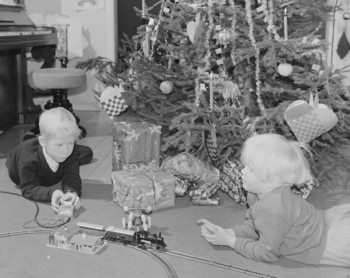 To barn foran juletre som leker med modelltog