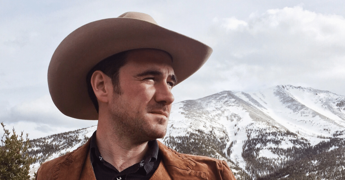 Mann i cowboyhatt, bakgrunn av snødekte fjell og skyer