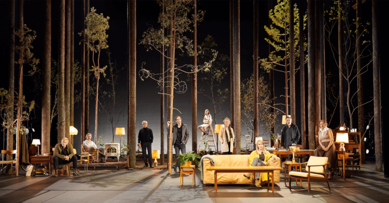 Et oppsett av Vildanden på Nationaltheatret. En sofa med en ung kvinne, høye trær i bakgrunnen på scenen.