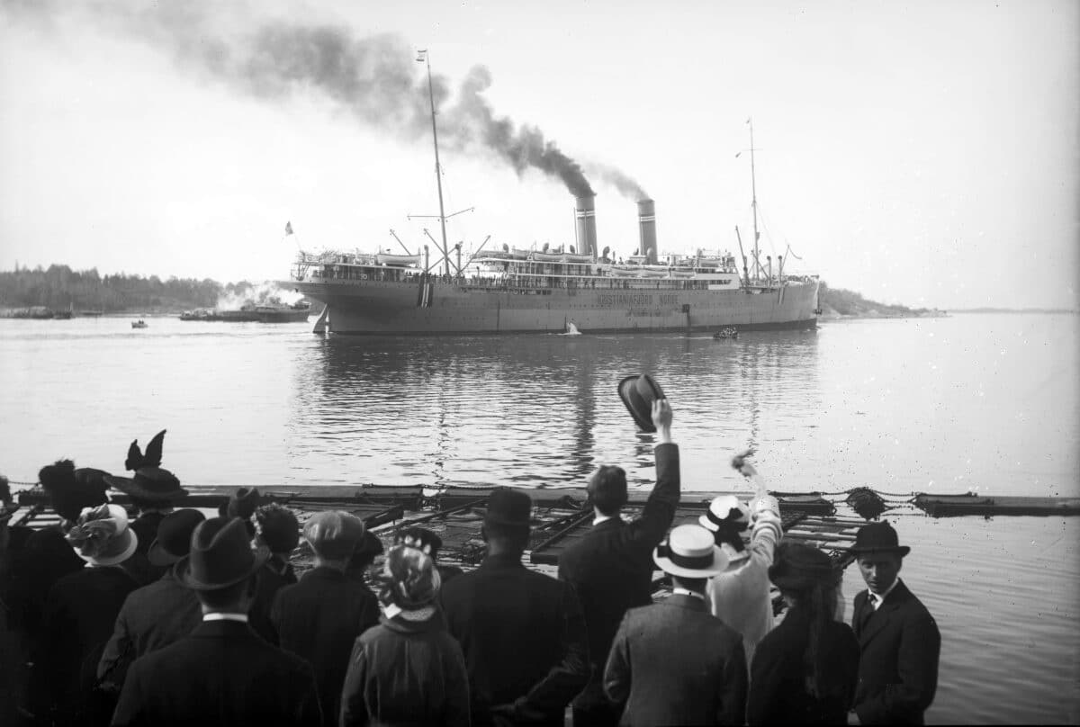 En dampbåt på havet. En større gruppe mennesker vinker farvel.