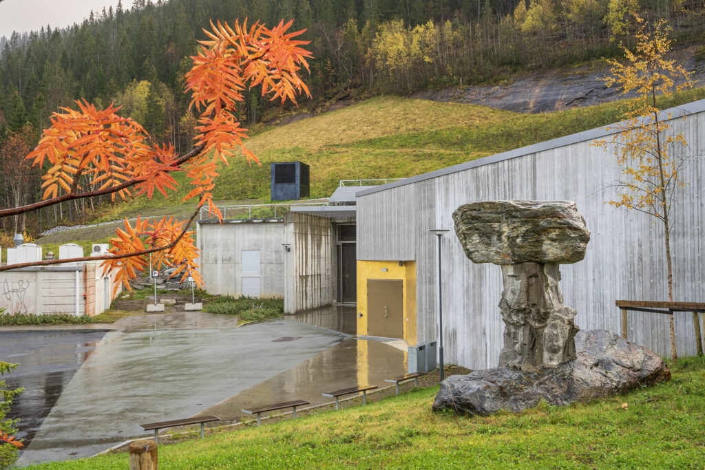 A concrete structure situated in the mountain side. Autumnal trees and colors in green and orange. 